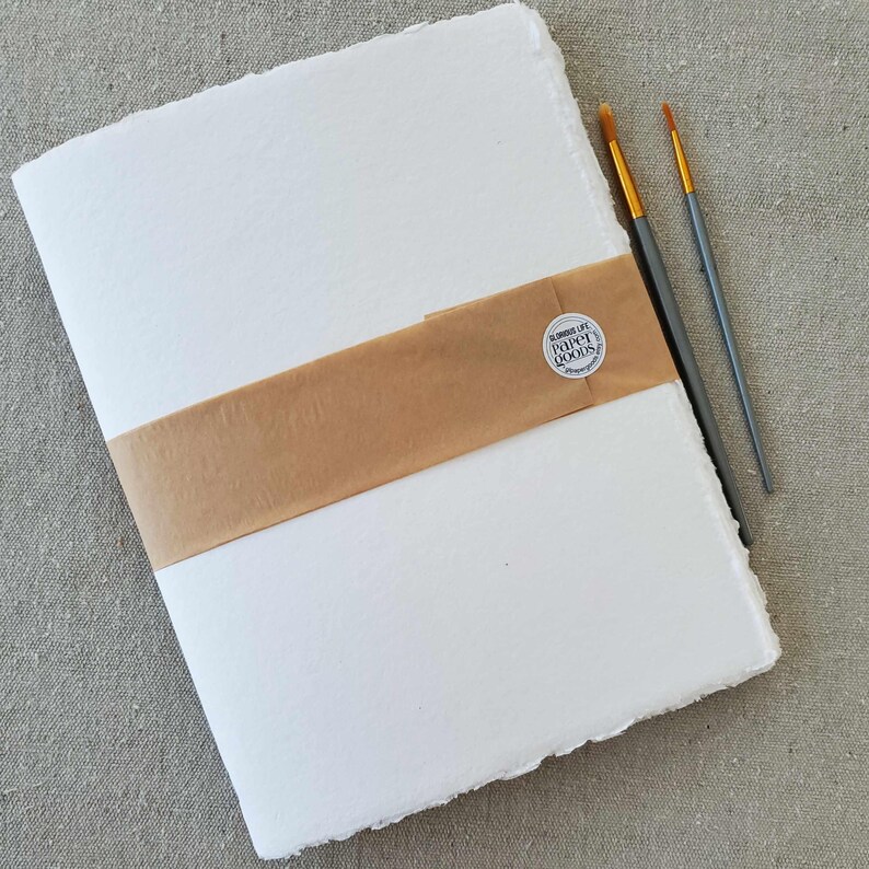 May include: A white, handmade paper journal with a brown paper band and a round sticker that says "Handmade by Paper Books".