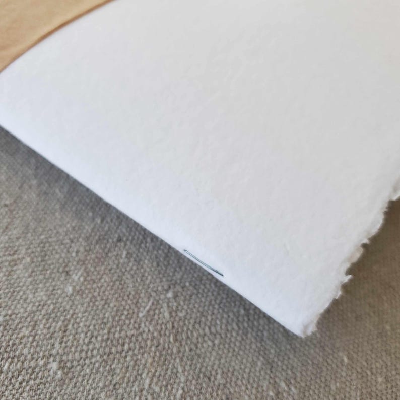 May include: A white notebook with a brown leather spine. The notebook is closed and has a single staple holding the pages together.