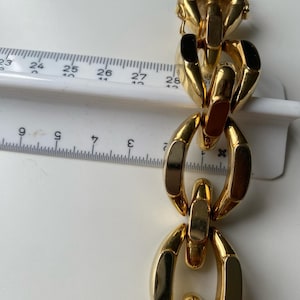 K&ouml;nnte beinhalten: Ein goldenes Kettenarmband mit gro&szlig;en, klobigen Gliedern. Die Glieder sind oval geformt und haben eine polierte Oberfl&auml;che.