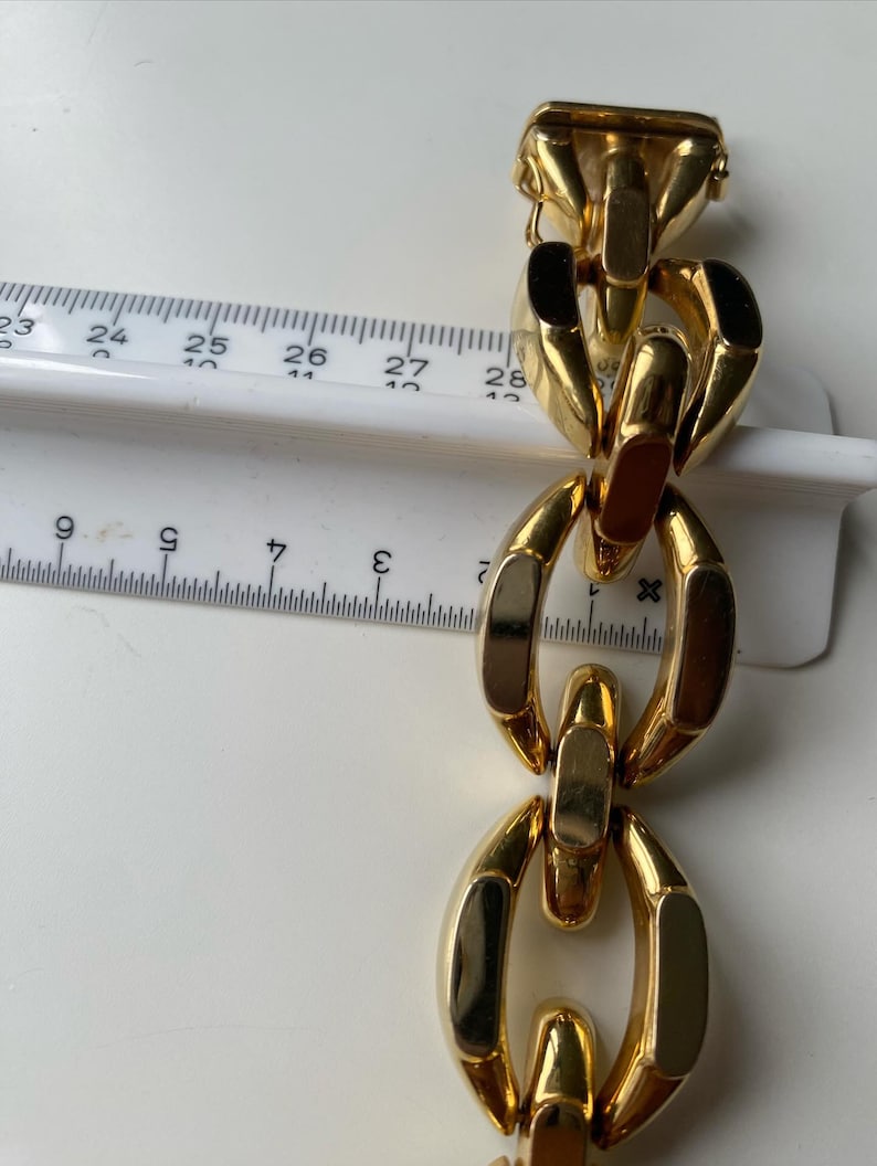 K&ouml;nnte beinhalten: Ein goldenes Kettenarmband mit gro&szlig;en, klobigen Gliedern. Die Glieder sind oval geformt und haben eine polierte Oberfl&auml;che.