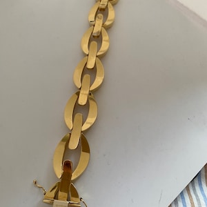 K&ouml;nnte beinhalten: Ein goldenes Kettenarmband mit einem einzigartigen ovalen Gliederdesign. Das Armband hat einen Verschluss.