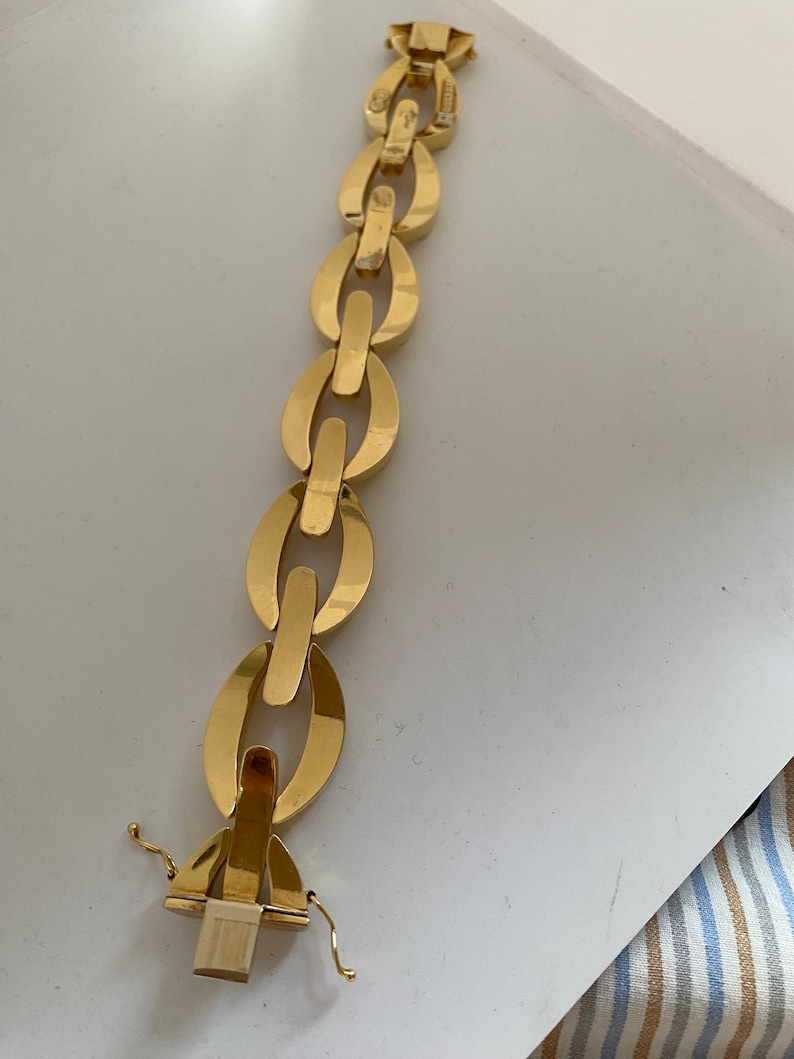 K&ouml;nnte beinhalten: Ein goldenes Kettenarmband mit einem einzigartigen ovalen Gliederdesign. Das Armband hat einen Verschluss.