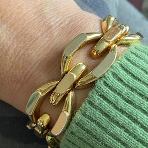 K&ouml;nnte beinhalten: Ein goldfarbenes Gliederarmband mit einem dicken Design. Das Armband ist aus Metall und hat eine polierte Oberfl&auml;che.