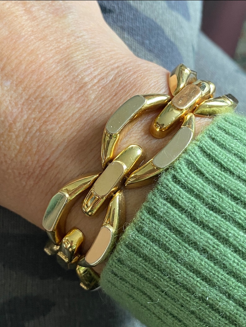 K&ouml;nnte beinhalten: Ein goldfarbenes Gliederarmband mit einem dicken Design. Das Armband ist aus Metall und hat eine polierte Oberfl&auml;che.