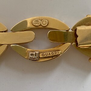 K&ouml;nnte beinhalten: Nahaufnahme eines goldenen Kettenarmbands mit den Worten "QUADRI" und "ITALY" auf dem Verschluss.