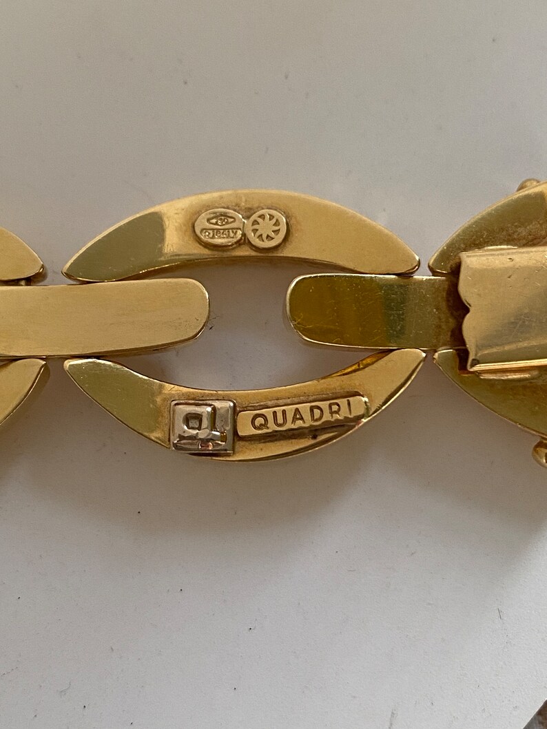 K&ouml;nnte beinhalten: Nahaufnahme eines goldenen Kettenarmbands mit den Worten "QUADRI" und "ITALY" auf dem Verschluss.