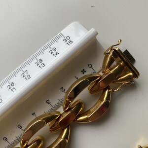 K&ouml;nnte beinhalten: Ein goldenes Kettenarmband mit gro&szlig;en, flachen, rechteckigen Gliedern. Das Armband ist etwa 6,5 cm breit und hat einen Verschluss.