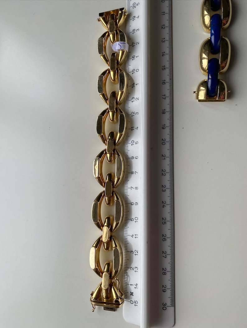 K&ouml;nnte beinhalten: Ein goldenes Kettenarmband mit einem Verschluss. Das Armband besteht aus ineinandergreifenden ovalen Gliedern. Das Armband wird an einem Lineal gemessen.