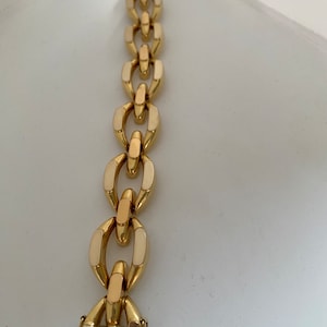 K&ouml;nnte beinhalten: Ein goldenes Kettenarmband mit wei&szlig;en Emaille-Akzenten. Das Armband hat einen Karabinerverschluss.