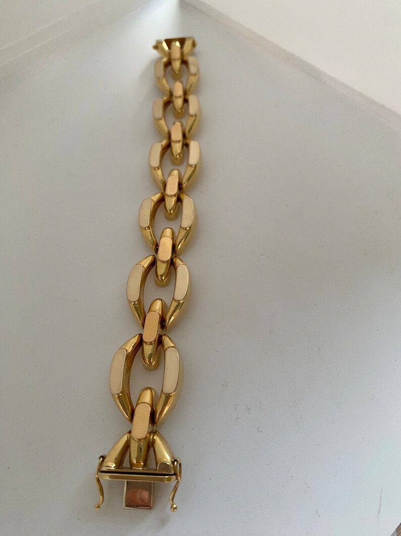 K&ouml;nnte beinhalten: Ein goldenes Kettenarmband mit wei&szlig;en Emaille-Akzenten. Das Armband hat einen Karabinerverschluss.