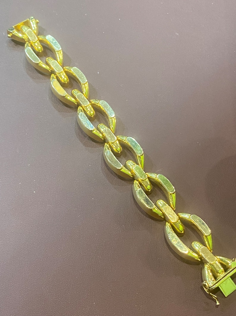 K&ouml;nnte beinhalten: Ein goldenes Kettenarmband mit einem einzigartigen Gliederdesign. Die Glieder sind oval geformt und haben eine strukturierte Oberfl&auml;che.