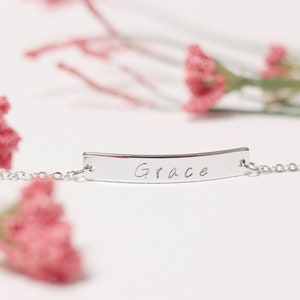 May include: Silver chain bracelet with a curved bar charm engraved with the name "Grace".