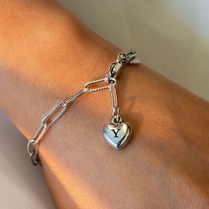 May include: A silver chain bracelet with a heart-shaped charm that has the letter "Y" engraved on it.