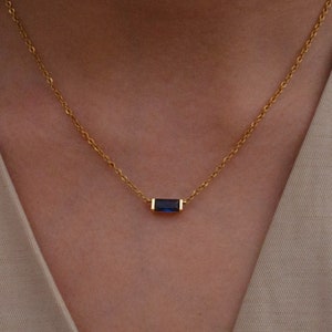 May include: A gold chain necklace with a small, rectangular blue gemstone pendant.