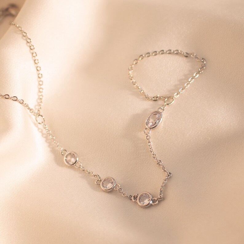 May include: A silver chain necklace with a silver ring attached. The necklace and ring have small clear stones.