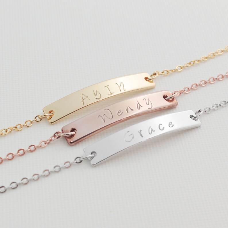 May include: Three gold, rose gold, and silver bar necklaces with the names Ayin, Wendy, and Grace engraved on them.