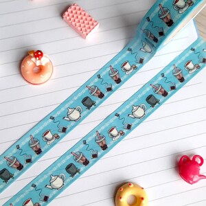 Pode incluir: Fita washi azul com um padr&atilde;o repetitivo de x&iacute;caras de ch&aacute;, bules e ch&aacute; de boba. A fita est&aacute; em um caderno branco com linhas e pequenos itens decorativos.