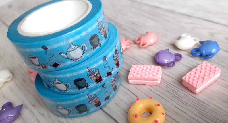 Pode incluir: Tr&ecirc;s rolos de fita washi azul com um tema de ch&aacute; e boba. A fita apresenta ilustra&ccedil;&otilde;es de bules, x&iacute;caras de ch&aacute;, ch&aacute; boba e saquinhos de ch&aacute;.