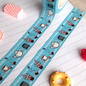 Pode incluir: Um rolo de fita washi azul com um padr&atilde;o repetido de x&iacute;caras de ch&aacute;, saquinhos de ch&aacute; e ch&aacute; de bolhas. A fita est&aacute; em um caderno branco com linhas.