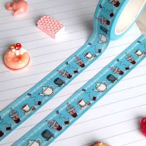 May include: A blue and white washi tape with a repeating pattern of teacups, teapots, and boba tea. The tape is on a white lined notebook with pink and yellow donuts and a pink waffle.