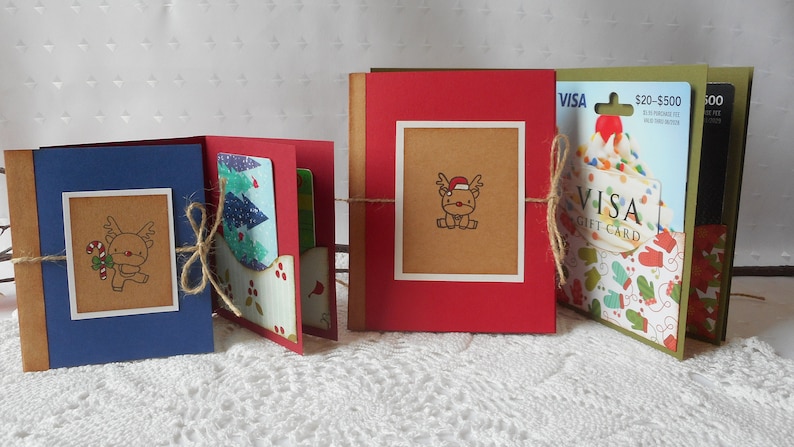 May include: Three handmade Christmas gift card holders with reindeer illustrations and twine accents. Each holder features a different colour scheme and design, including blue, red and green.