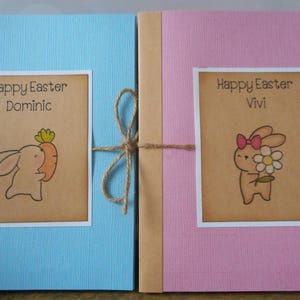 May include: Two blue and pink Easter cards with brown paper wrapping and twine. The cards feature a bunny illustration and the text "Happy Easter Dominic" and "Happy Easter Vivi".