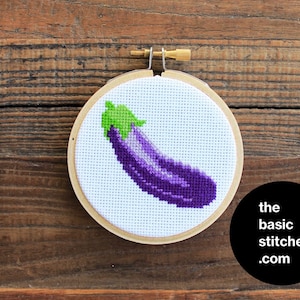 May include: A purple and green embroidered eggplant cross-stitch pattern in a wooden embroidery hoop.