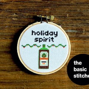 May include: A white embroidery hoop with a green and red embroidered design of a bottle of liquor with the text "holiday spirit".