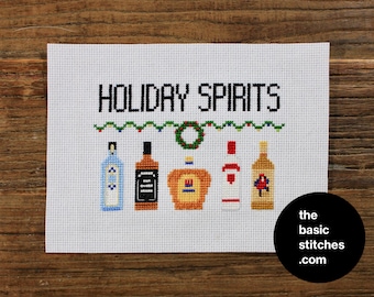 Puede incluir: Patrón de punto de cruz con la frase "Holiday Spirits" con una guirnalda de luces verdes y rojas y cinco botellas de licor, incluyendo una botella de ginebra, whisky, whisky canadiense, vodka y ron. El patrón está en tela Aida blanca.