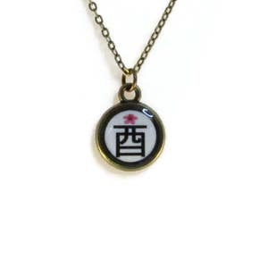 May include: A gold chain necklace with a round pendant featuring a white background with a black kanji character and a pink flower. The pendant has a gold rim.