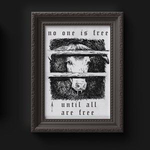 Puede incluir: Impresión artística enmarcada en blanco y negro. La obra de arte representa una vaca, dividida en tres secciones, con el texto "no one is free until all are free." El marco es gris oscuro con un diseño ornamentado.