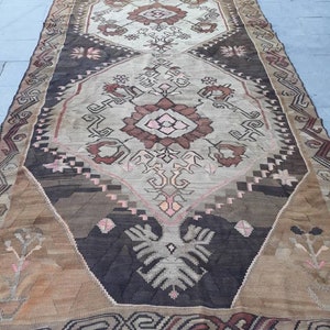 May include: A vintage Turkish rug with a geometric pattern in shades of brown, beige, and pink. The rug has a fringed edge and is woven with intricate details.