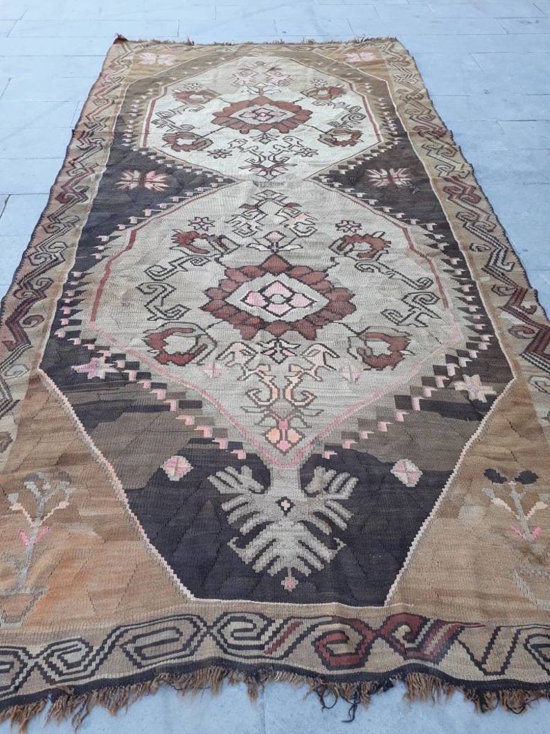 May include: A vintage Turkish rug with a geometric pattern in shades of brown, beige, and pink. The rug has a fringed edge and is woven with intricate details.