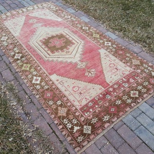 May include: A vintage Turkish rug with a red, cream, and brown color scheme. The rug has a geometric pattern with a central medallion and a floral border.