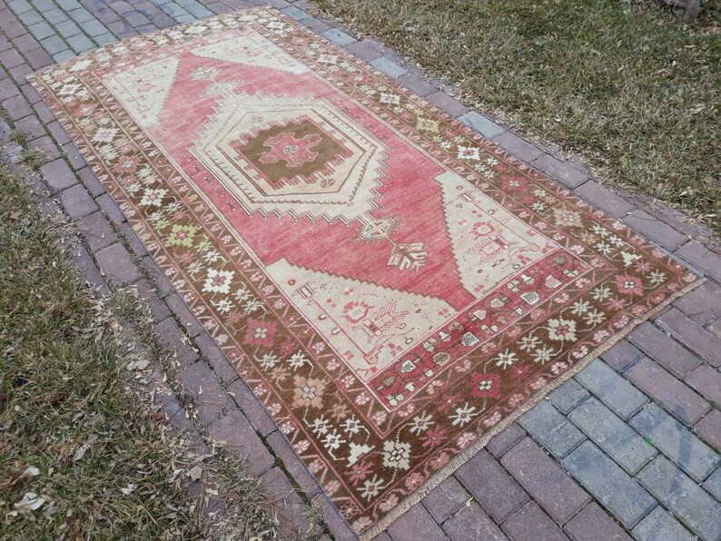 May include: A vintage Turkish rug with a red, cream, and brown color scheme. The rug has a geometric pattern with a central medallion and a floral border.