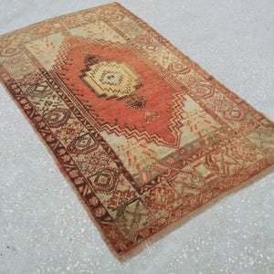 May include: A vintage rug with a red, white, and brown geometric pattern. The rug has a fringed edge and is made of wool.