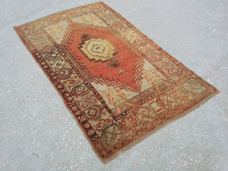 May include: A vintage rug with a red, white, and brown geometric pattern. The rug has a fringed edge and is made of wool.
