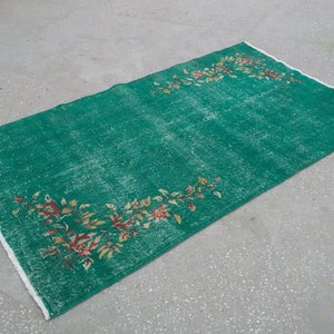 Pode incluir: Um tapete verde vintage com um padr&atilde;o floral em tons de vermelho, amarelo e branco. O tapete tem um aspecto desgastado e &eacute; franjado em todos os lados.