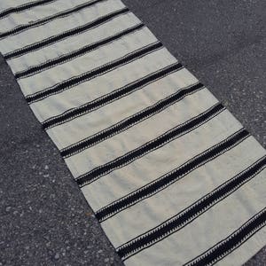 Pu&ograve; includere: Un tappeto a strisce bianche e nere con un design intrecciato. Il tappeto &egrave; realizzato in un materiale morbido e naturale e ha un aspetto semplice ed elegante.