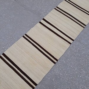 May include: A white and brown striped runner rug with fringe on the ends. The rug is made from a natural fibre and has a simple, classic design.