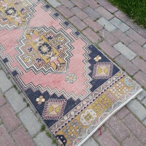 May include: A pink and yellow patterned runner rug with a dark blue border. The rug is laid out on a brick walkway.