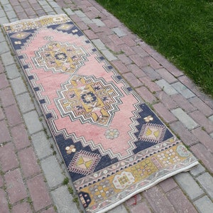 May include: A pink and cream runner rug with a geometric pattern in shades of yellow, black, and cream. The rug has a fringed edge.