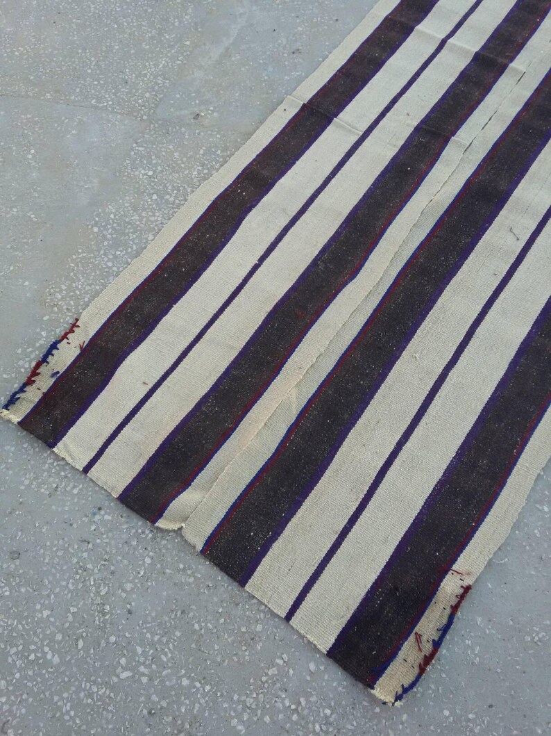 May include: A white and dark brown striped rug with a red and blue accent. The rug is woven and has a rough texture.