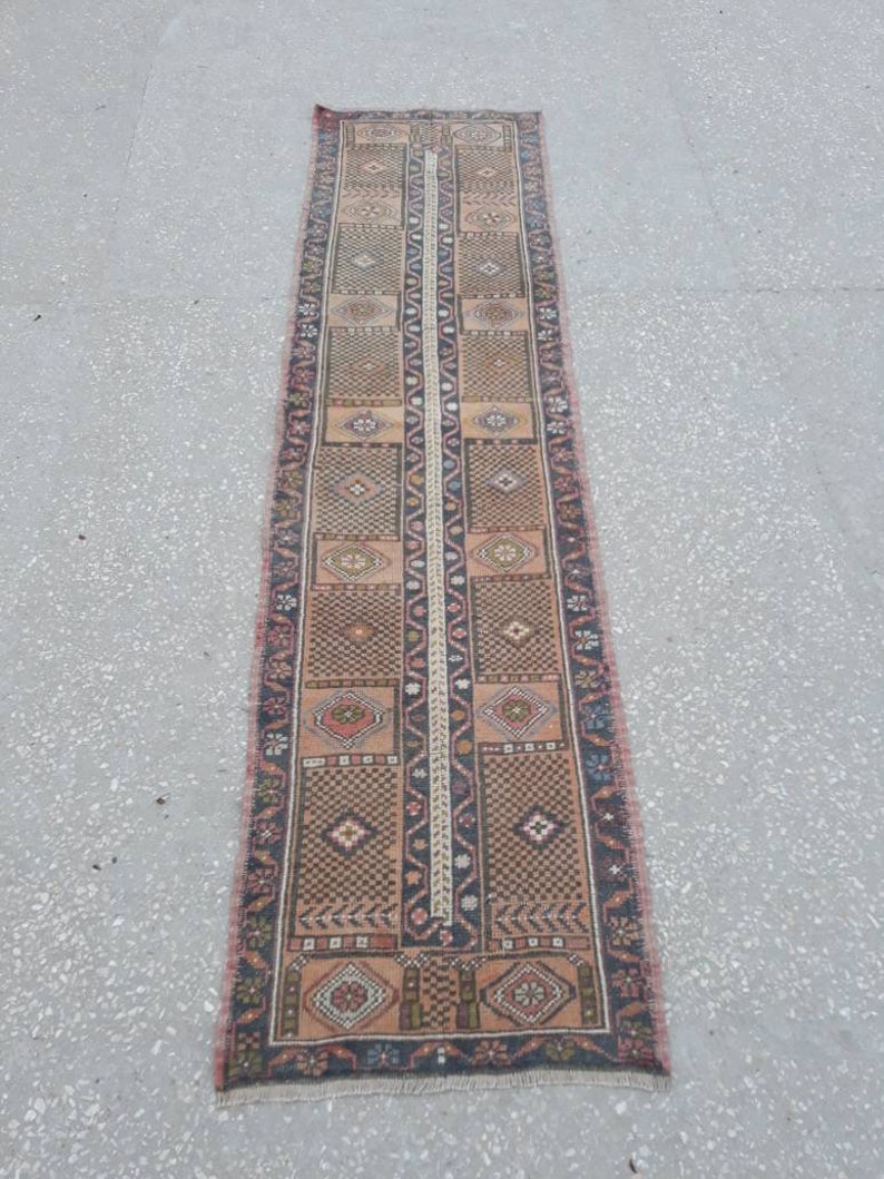 May include: A long, narrow rug with a traditional Persian design. The rug is primarily beige with brown, red, and black accents. The rug has a fringe on both ends.
