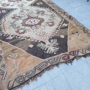 May include: A vintage rug with a geometric pattern in shades of brown, beige, and pink. The rug has a fringe border and is made of wool.