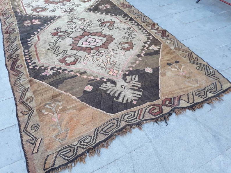 May include: A vintage rug with a geometric pattern in shades of brown, beige, and pink. The rug has a fringe border and is made of wool.