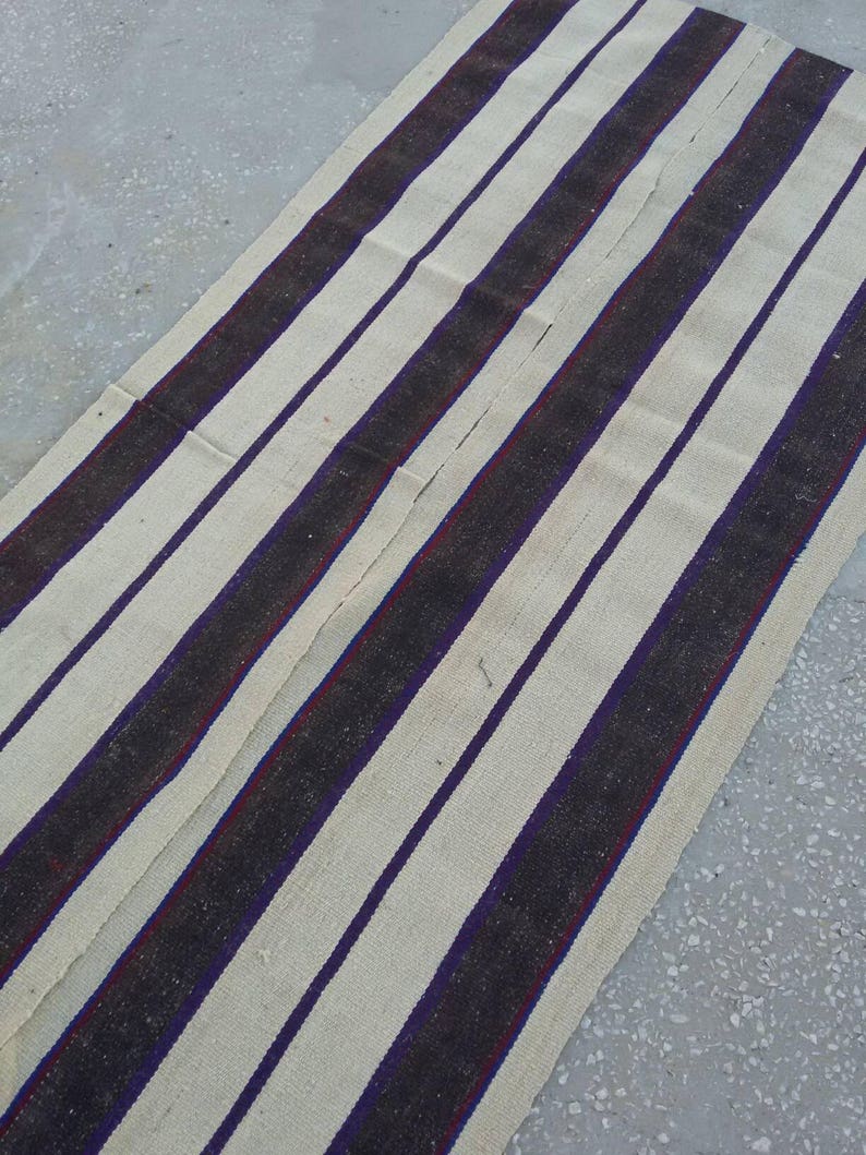 May include: A white and black striped rug with a subtle purple stripe. The rug is made of a woven fabric and has a rustic, vintage look.