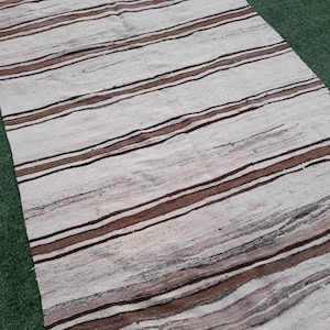 May include: A white and brown striped rug with a woven texture. The rug has a long, rectangular shape and is made of natural fibres.