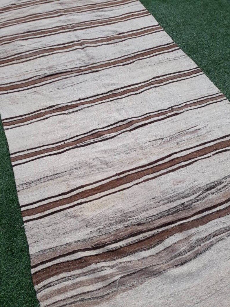 May include: A white and brown striped rug with a woven texture. The rug has a long, rectangular shape and is made of natural fibres.