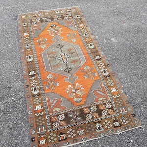 May include: A vintage Turkish rug with a geometric pattern in shades of orange, brown, and gray. The rug has a central medallion and a border with intricate designs.